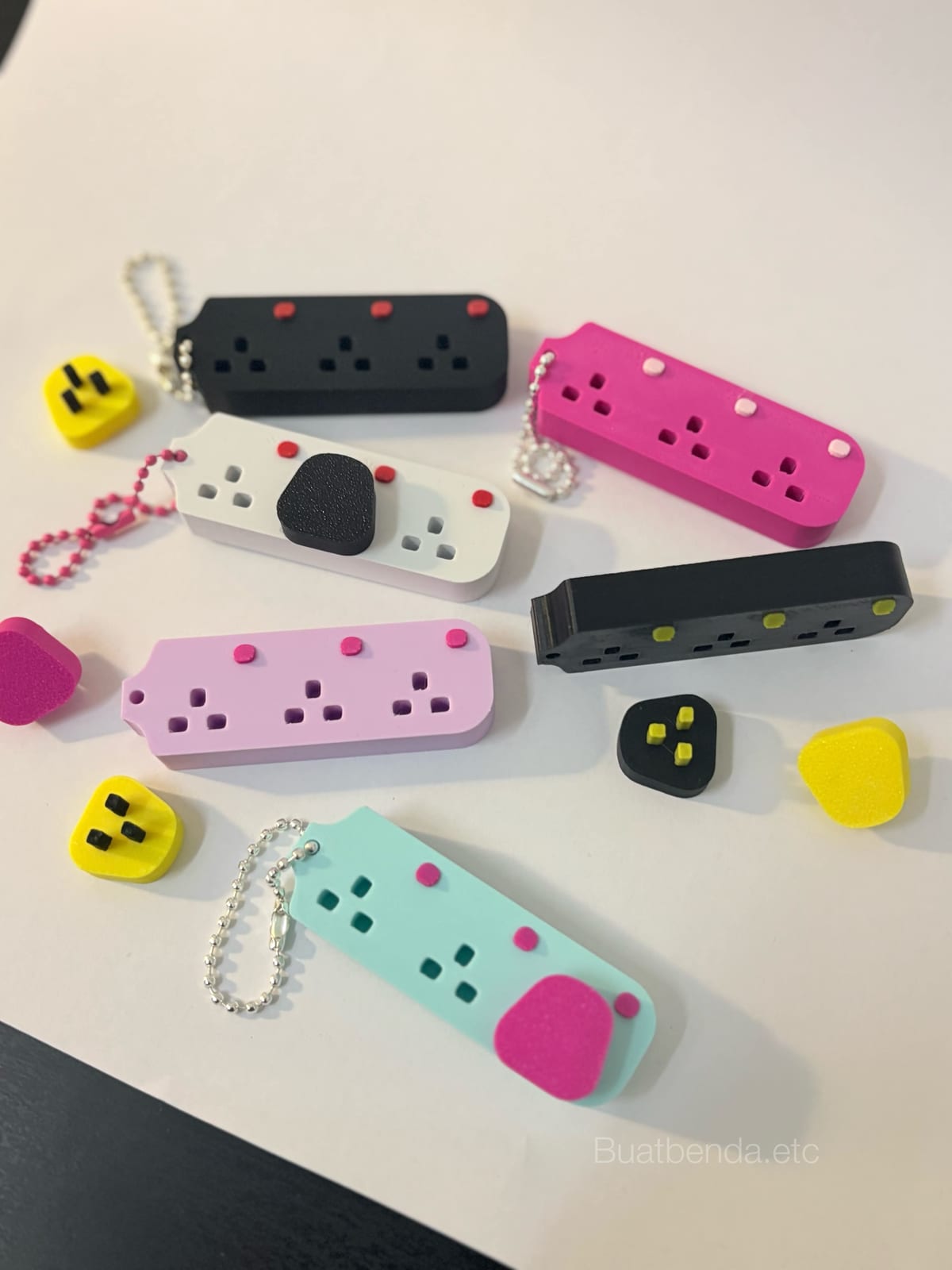 Extension plug keychains in several colours laid out on a table